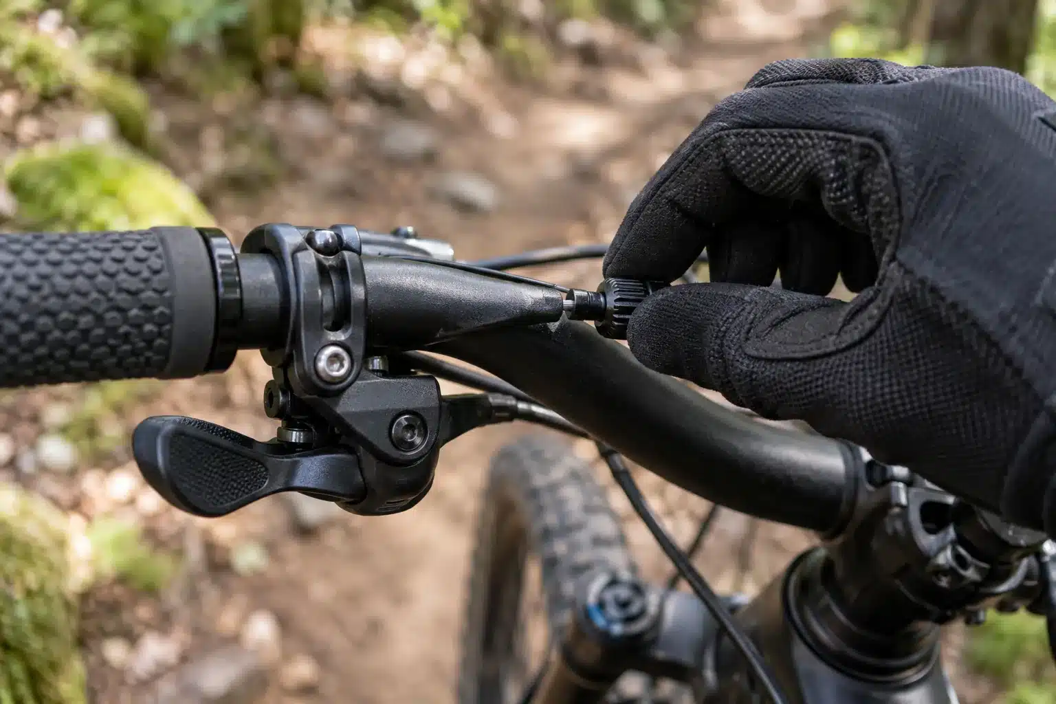 Main gantée qui tourne la molette de réglage de tension du câble de frein à la sortie du levier, sur un guidon de VTT