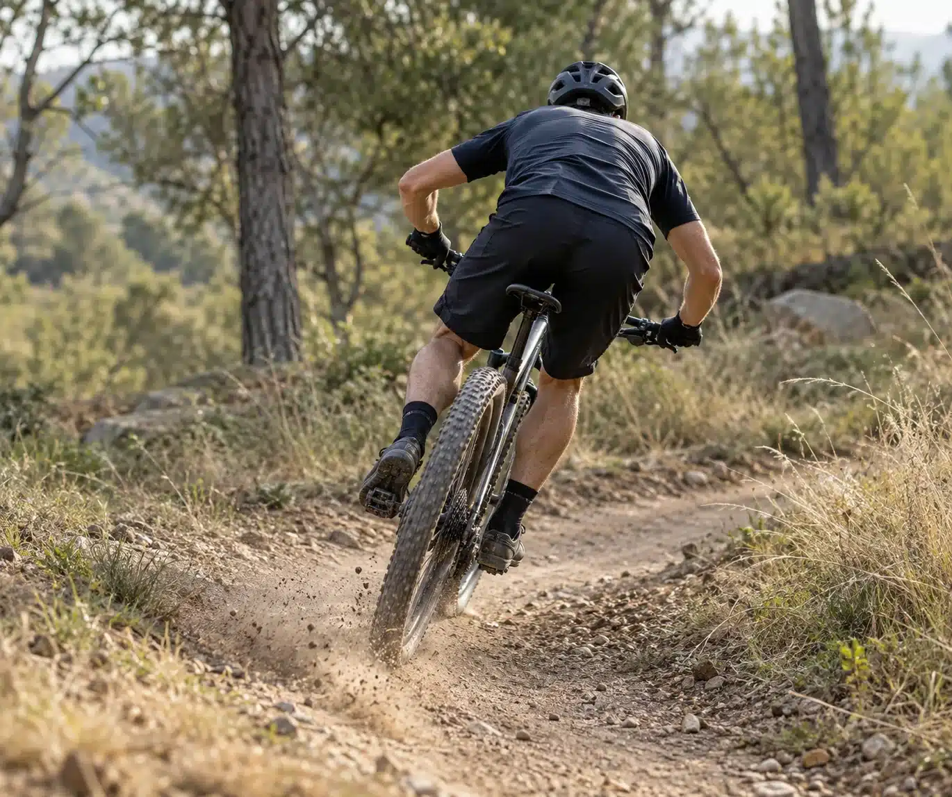 Vue arrière d'un pilote de VTT XC qui se redresse et relance à la sortie d'un virage à plat, poussière projetée par la roue arrière